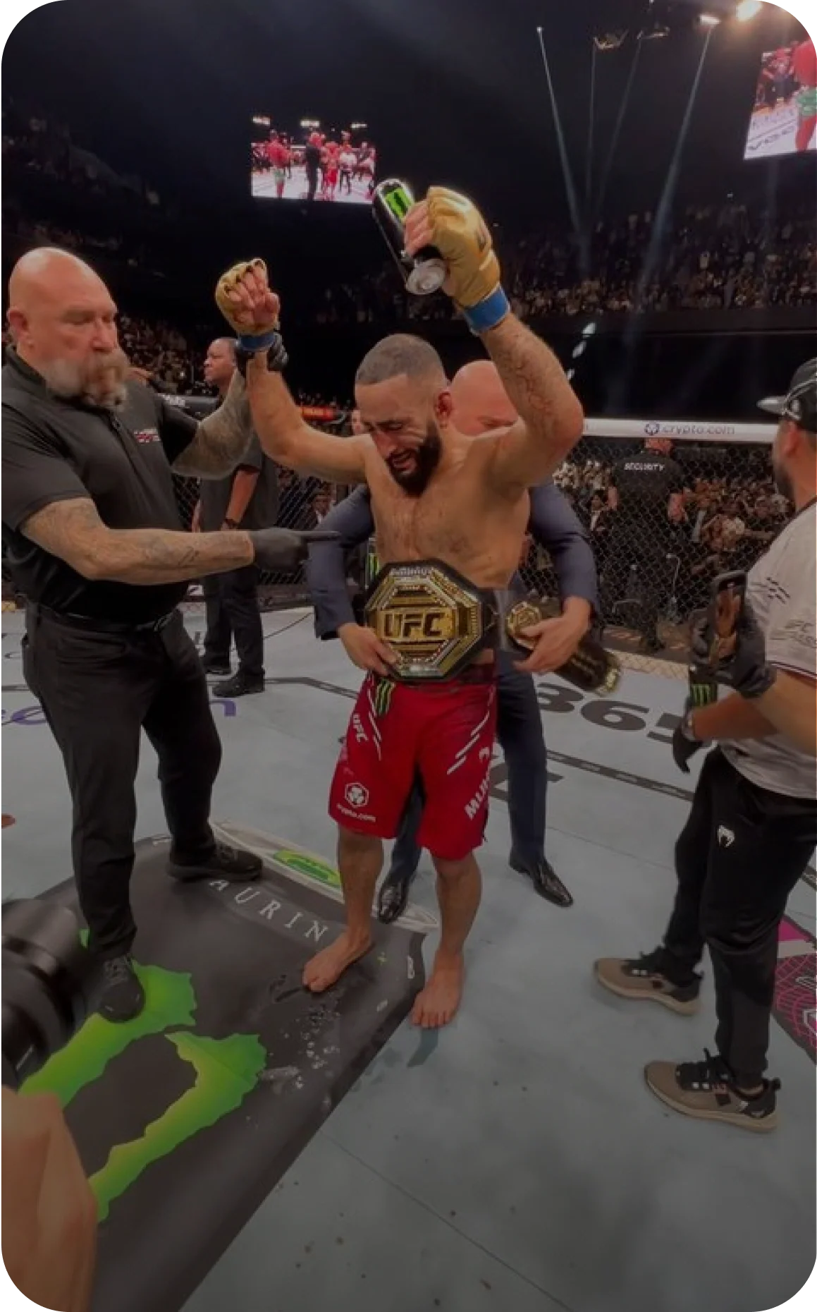 Photo of a man celebrating in a UFC fighting ring while raising his arms, wearing a championship belt, labeled as Belal Muhammad, 2x UFC World Champion.